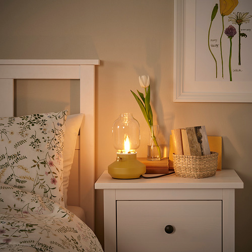 Acogedor rincón de dormitorio con lámpara TÄRNABY, tulipanes y libros.