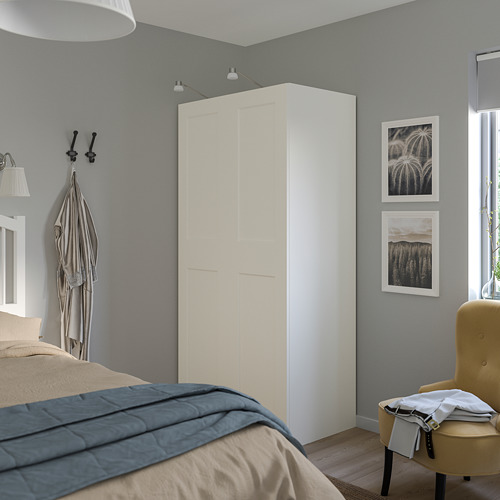 Alt: armario PAX blanco con ropa de cama y silla.