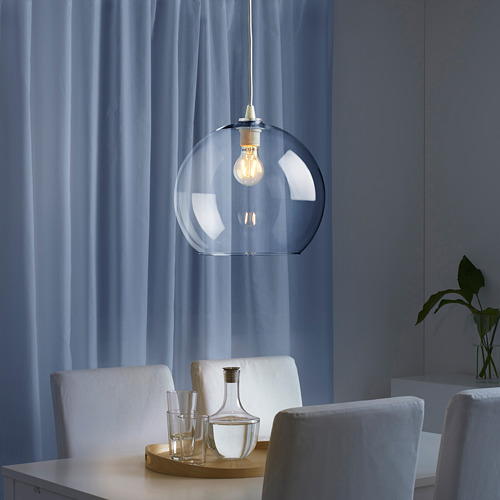 Lámpara colgante con pantalla de vidrio, bombilla encendida, encima de la mesa con sillas y cristalería.