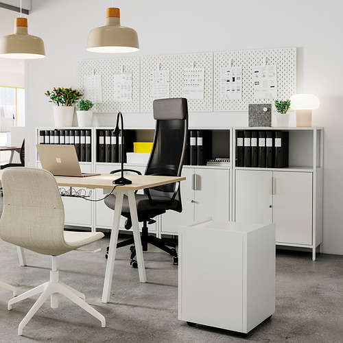 Moderna oficina con armario de almacenaje blanco TROTTEN con silla de malla negra y escritorio de madera clara. Organizado con carpetas, plantas y lámparas colgantes.