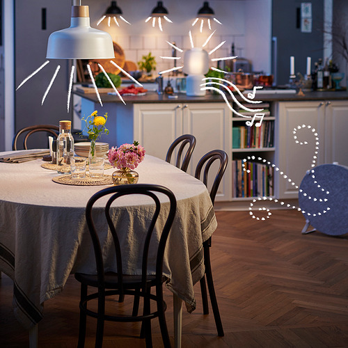 Comedor moderno con lámparas colgantes, flores y jarrones en la mesa, cocina acogedora adyacente con suelos de madera.