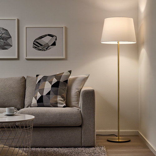 Sala de estar minimalista con sofá gris, lámpara de pie moderna, pantalla de lámpara crema, mesa de centro y arte abstracto en la pared.