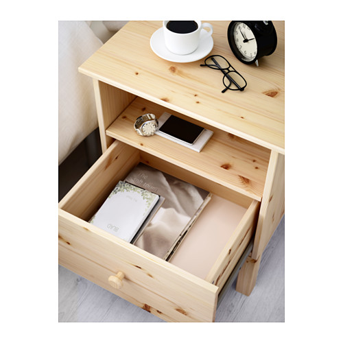 Mesita de noche de madera con cajón abierto que muestra el libro y el reloj; Estante superior con vasos, reloj y taza de café.