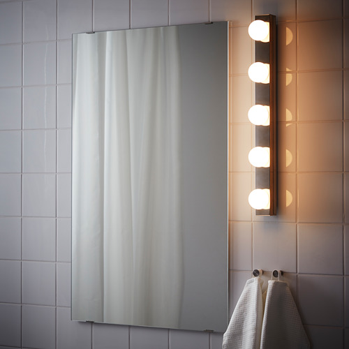 Espejo con luces en pared de azulejos. Cuatro bombillas para un aseo brillante. Las toallas cuelgan al lado.