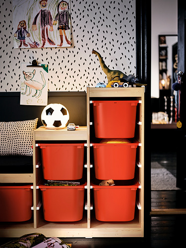 Una habitación para niños con contenedores de almacenamiento de juguetes rojos, una mesa de madera y coloridas obras de arte en papel tapiz de lunares, con una pelota de fútbol y un dinosaurio de juguete.