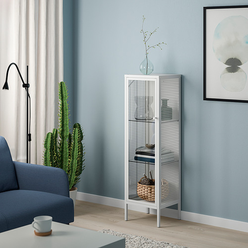 Sala de estar moderna con vitrina de metal blanco BAGGEBO que muestra la decoración. Junto a un sillón azul y un cactus, contra una pared celeste.