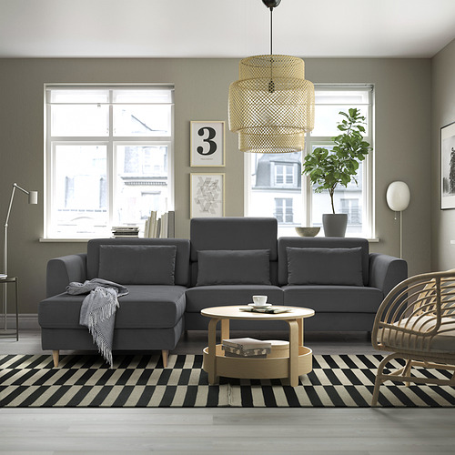 Sala de estar moderna con seccional SLATORP gris, alfombra en blanco y negro, mesa de centro de madera, silla de mimbre, grandes ventanales y elegante lámpara colgante.