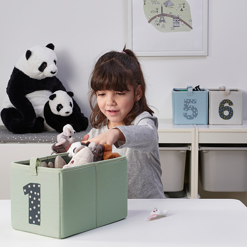 Una niña organiza los juguetes en una caja de almacenamiento de tela etiquetada, aprendiendo a contar mientras mantiene su habitación ordenada.