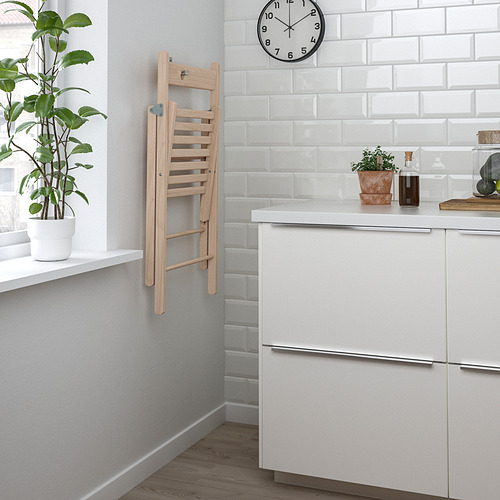 La silla de cocina plegable de madera se cuelga en la pared, ahorrando espacio. Cocina blanca con plantas y reloj.