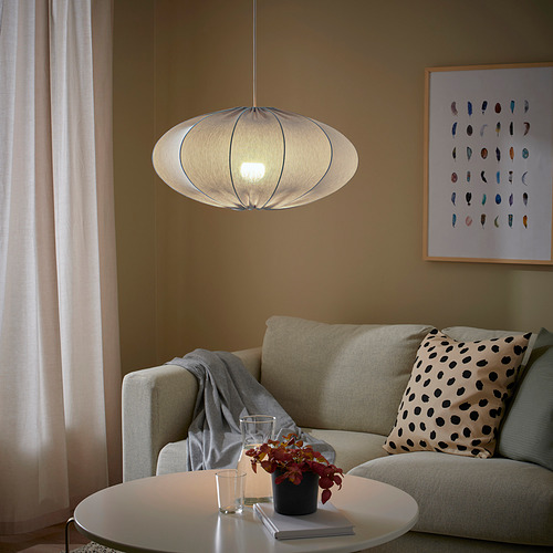 Sala de estar moderna con lámpara REGNSKUR, sofá beige, almohadas, manta, mesa de café, libro, planta y colorido arte plumario.