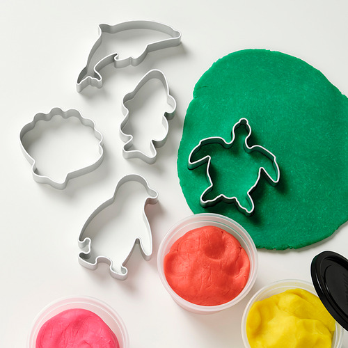 Plastilina con cortadores: un cortador de tortuga presiona la masa verde, rodeada de varios otros cortadores y recipientes de plastilina de colores.
