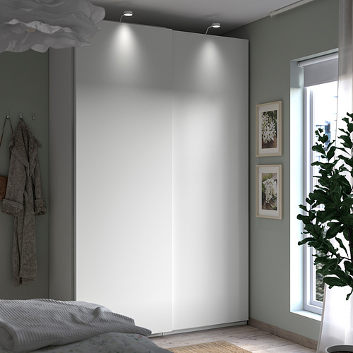Dormitorio minimalista con armario blanco PAX, paredes grises, luz natural por ventana, arte enmarcado y planta interior.