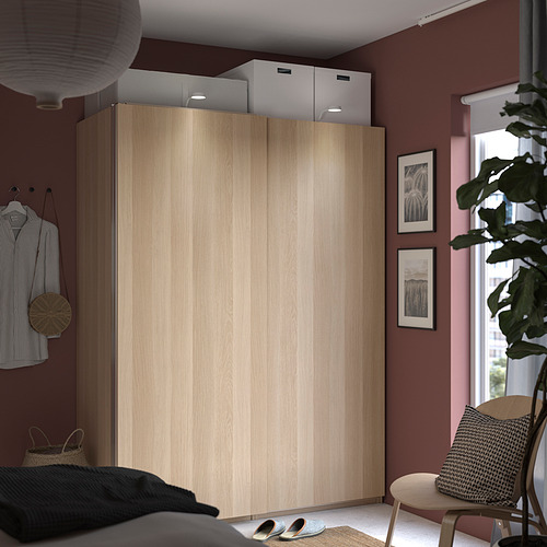 Dormitorio moderno con armario beige PAX, cajas blancas, planta verde, almohadas en blanco y negro, camisa a rayas y marcos de arte.