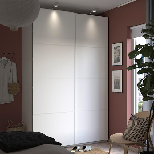 Dormitorio moderno con armario PAX blanco, pared roja, planta en maceta, camisa a rayas, zapatillas, silla de madera.