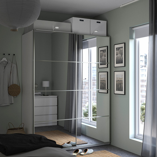 Dormitorio moderno con armario PAX con puertas correderas con espejos, cofre de tela gris al lado y estantes blancos con almacenamiento en caja arriba.