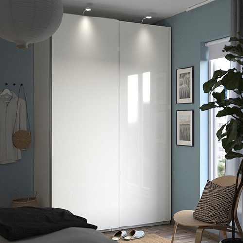 Habitación moderna con armario corredero HASVIK blanco brillante, abrigo colgante, silla, planta y gran ventanal.