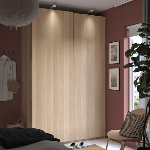 Dormitorio con gran armario de madera PAX, plafones encendidos, camisa a rayas colgada, planta grande y decoración moderna.