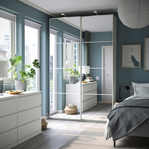 Dormitorio moderno con armarios PAX blancos con puertas correderas con espejos, ropa de cama gris, paredes azul verdosa y suelos de madera con alfombra tejida.