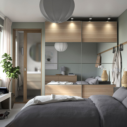 Dormitorio gris moderno con armario PAX, paneles de madera, puertas de cristal, ropa tendida, ganchos de pared y una planta.