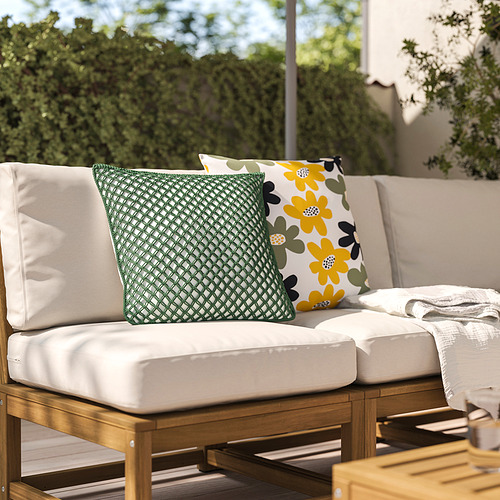 Silla acolchada blanca con cojines de diamantes verdes y flores amarillas, rodeada de vegetación.