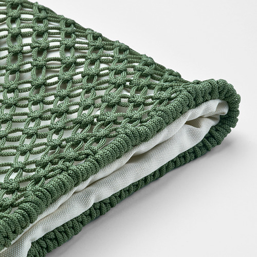 Se muestra una funda de cojín de ganchillo verde, doblada cuidadosamente, con un patrón intrincado y forro interior blanco.