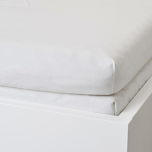 Sábana bajera blanca sobre cama blanca, mostrando laterales y esquinas elásticas.