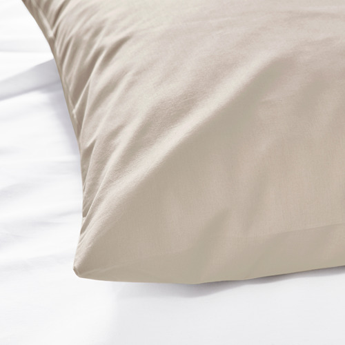 Funda de almohada beige y lisa sobre una cama, que muestra una textura de algodón suave y de alta calidad.