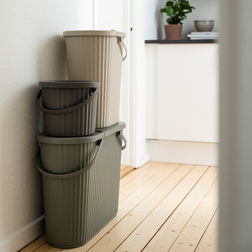 Tres papeleras DAMMÄNG apiladas en tonos beige y gris, rectangulares con asas, perfectamente encajadas contra la pared en una habitación moderna y minimalista.