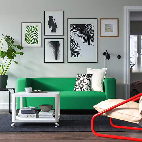 Luminoso salón con sofá KLIPPAN verde, estampados de moda, mesa kartell blanca y silla roja.