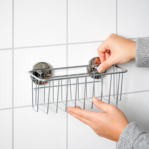 Una persona instala un carrito de ducha plateado KROKFJORDEN con ventosas en una pared de azulejos.