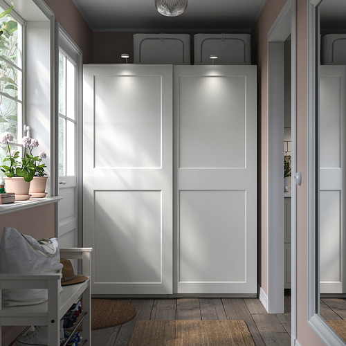 Un armario PAX blanco con puertas correderas, con iluminación integrada y una cesta de malla para almacenamiento.