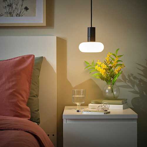 Acogedor rincón de dormitorio con lámpara SUNNEBY, libros, flores y almohadas cálidas.
