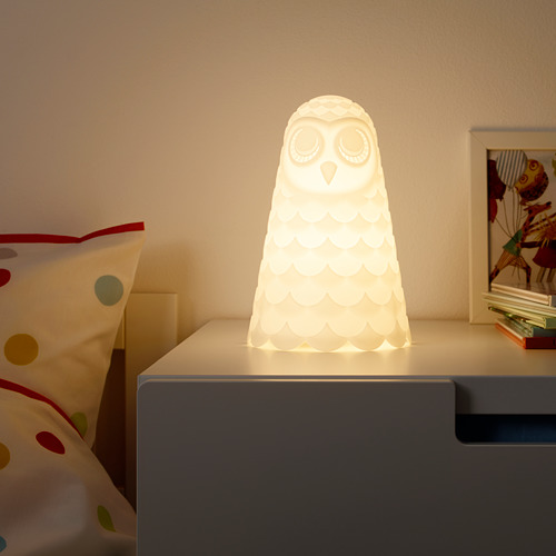 Luz nocturna en forma de búho en una mesita de noche, que proporciona una suave luz ambiental.