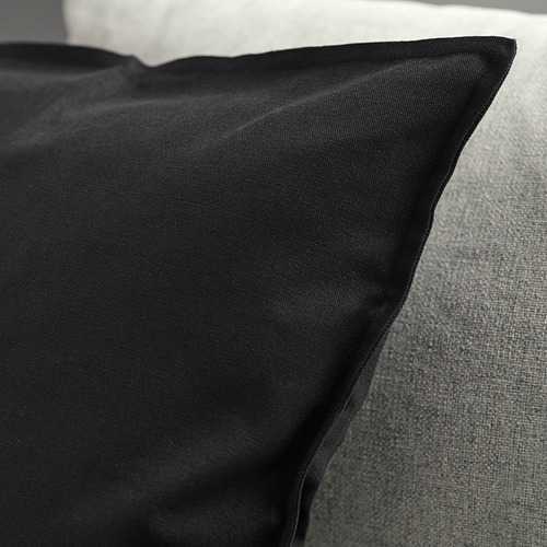 Funda de almohada negra sobre sofá gris, textura lisa, cremallera visible.