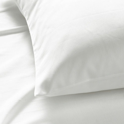 Primer plano de una lujosa funda de almohada lisa. Blanco impoluto, tela suave y satinada, vislumbre sábanas frescas debajo.