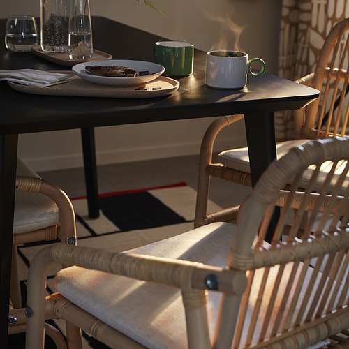 Acogedora configuración de comedor con silla SALNÖ en ratán claro junto a la mesa con tazas, platos y vasos.