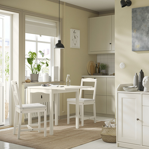 Comedor moderno y acogedor con mesa y sillas de madera blanca. Una lámpara colgante, una planta en maceta y decoración en las paredes.
