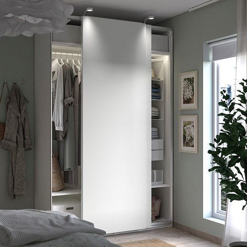 Dormitorio con armario PAX blanco abierto que revela ropa, estantes y almacenamiento; Paredes grises y ventana con planta.