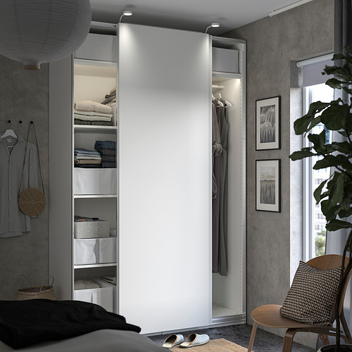 Dormitorio moderno con armario PAX blanco, cuadros enmarcados, silla de madera y plantas.