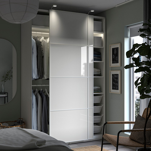 Dormitorio moderno con armario PAX blanco, puertas correderas, iluminación incorporada y ropa organizada.