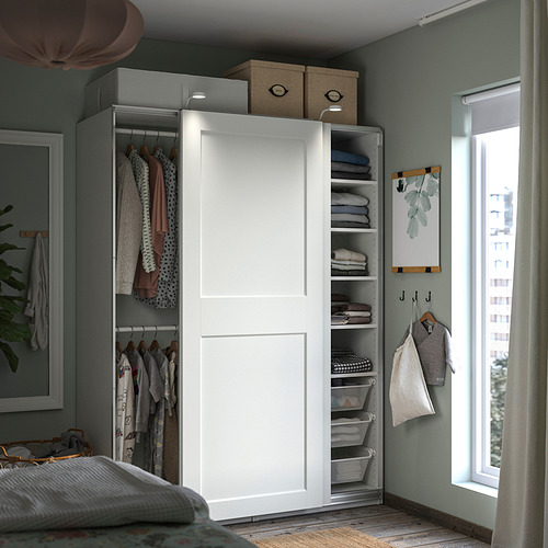 Dormitorio ordenado con armario PAX blanco, ropa y estantes. Paredes verdes, con luz natural por ventana y cortinas.
