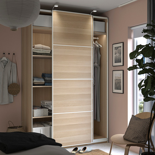 Dormitorio moderno con armario de madera PAX, paredes rosas, plantas y arte.