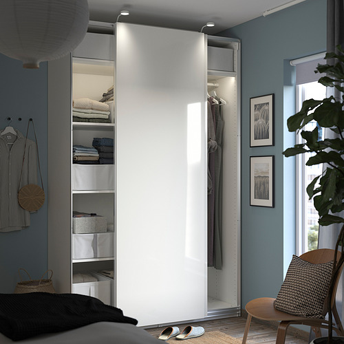 Moderno dormitorio azul con armario PAX blanco, puertas correderas y estantes. La silla y las plantas de interior también son visibles.