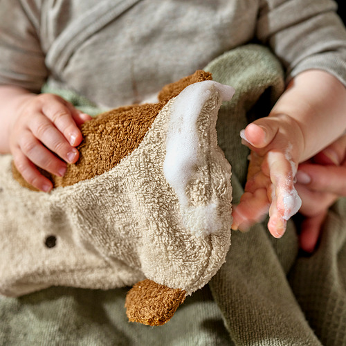 Niño sosteniendo un guante de lavado beige con forma de jirafa GULDVÄVARE. Algodón orgánico suave con cara bordada, perfecto para una limpieza suave.