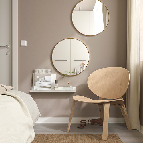 Dormitorio minimalista con espejo LINDBYN dorado, sala reflectante. Silla de madera clara, escritorio con vela, revista, tonos tranquilos.