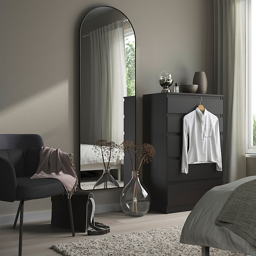 Dormitorio moderno con espejo negro alto, tocador y silla acogedora.