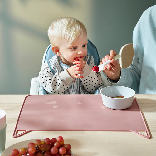 Bebé comiendo fruta en silla alta con uvas cerca.