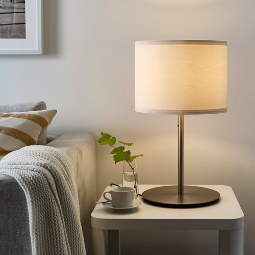 Lámpara minimalista moderna en mesita de noche junto a una cama acogedora, con taza, planta y marco.