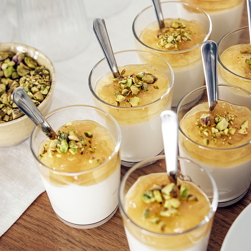 Pequeños vasos rellenos de postre cubiertos con pistachos y cucharas; Perfecto para servir postres.