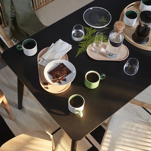 Moderno juego de comedor con mesa LISABO y sillas de madera clara, con platos, tazas, plantas y una cafetera.
